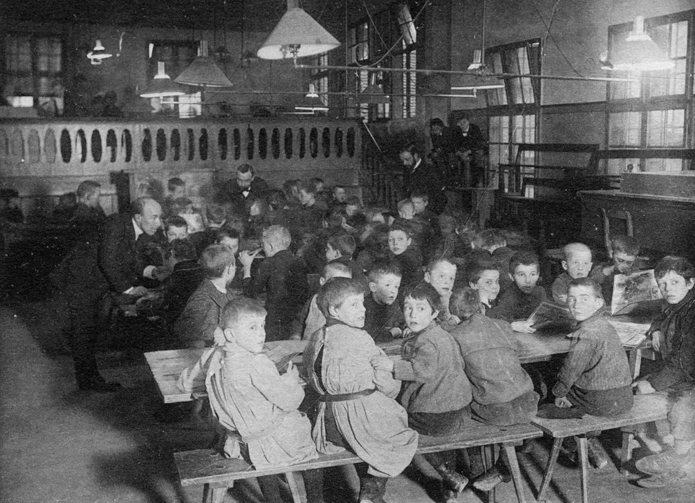 historische Aufnahme von Kindern und Betreuern an Tischen