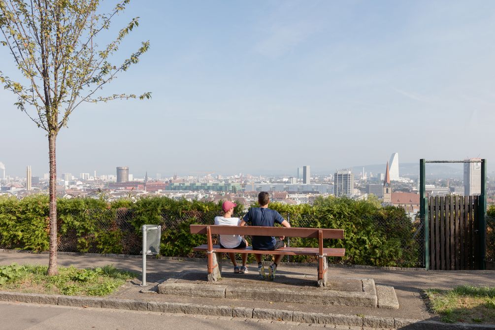 Ein Paar sitzt auf einer Parkbank mit Blick auf die Stadt Basel.