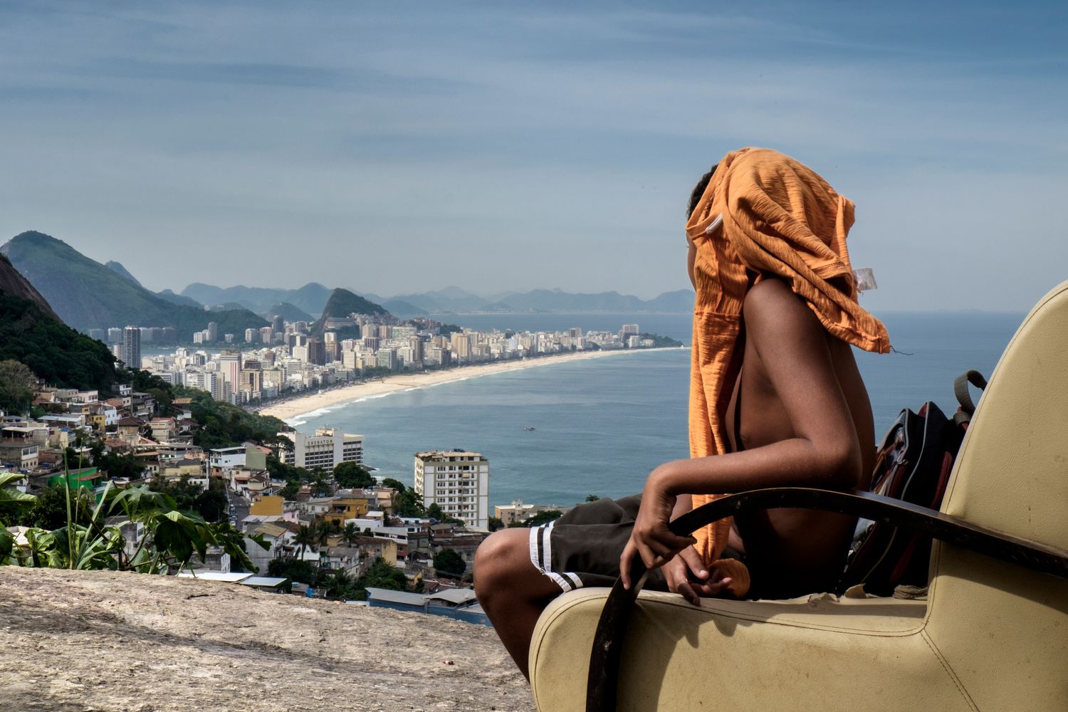 Ein dunkelhäutige Junge aus der Favela Vidigal sitzt auf einem Sessel und blickt auf den Strand von Rio de Janeiro. 
