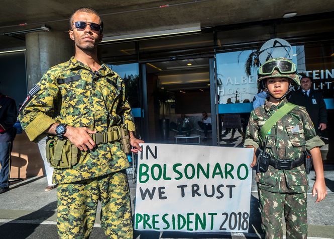 Ein Mann und ein kleiner Junge in Kampfausrüstung zeigen mit einem Plakat, das sie Bolsonaro für die kommende Präsidentschaftswahl ihr Vertrauen schenken.