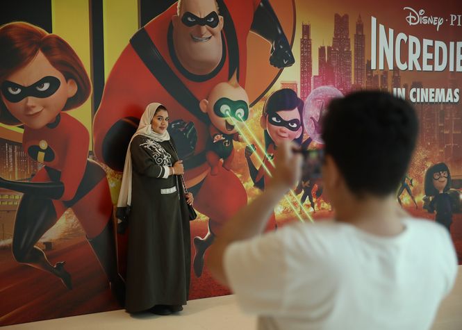 Eine Frau lässt sich von ihrem Sohn vor einem Werbeplakat des Kinofilm "Incredibles" fotografieren.