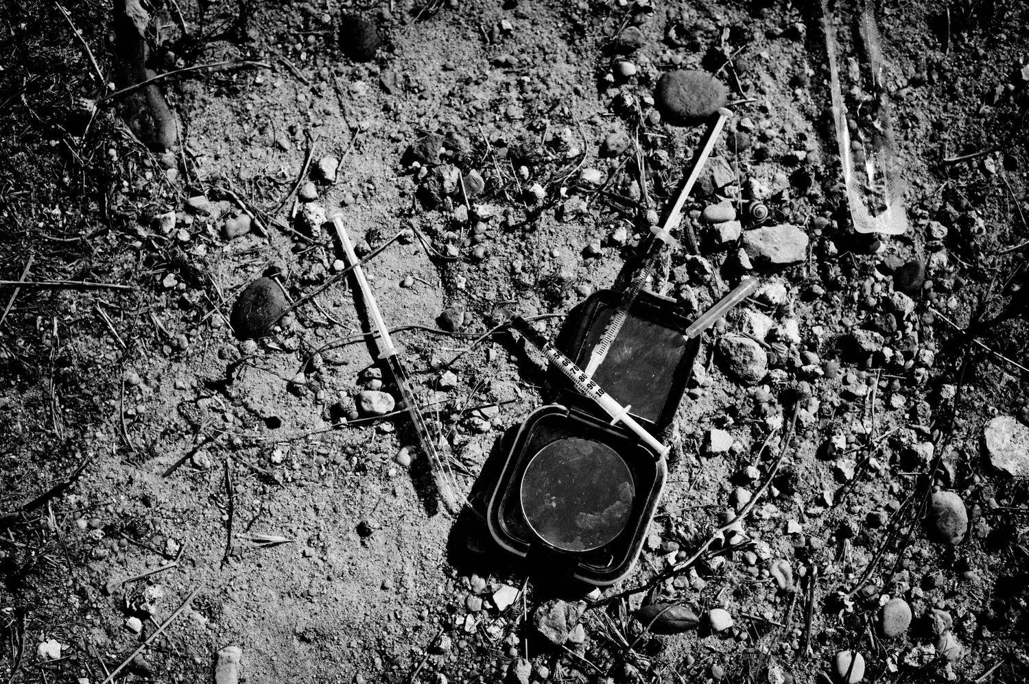 Schwarzweiss Fotografie zeigt gebrauchte Spritzen am Boden.