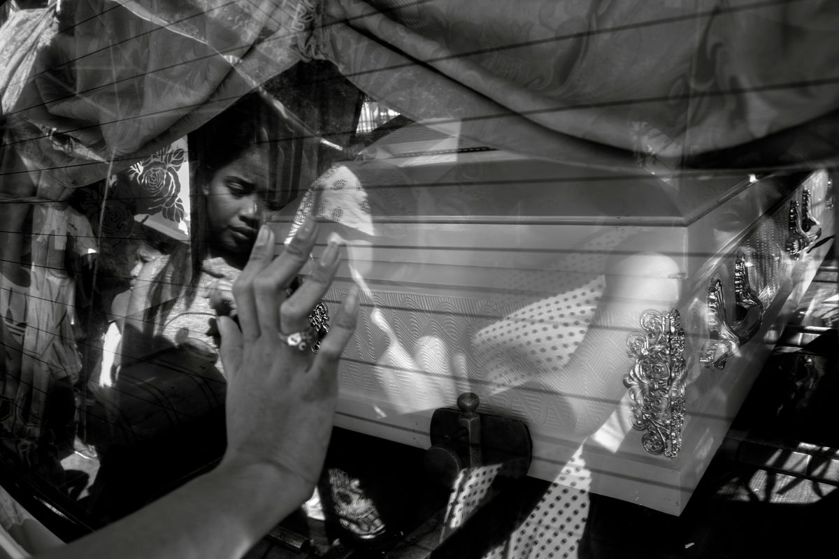 Ein Hand berührt das Fenster eines Leichenwagens, in der Spigelung das Gesicht eines trauernden Mädchens