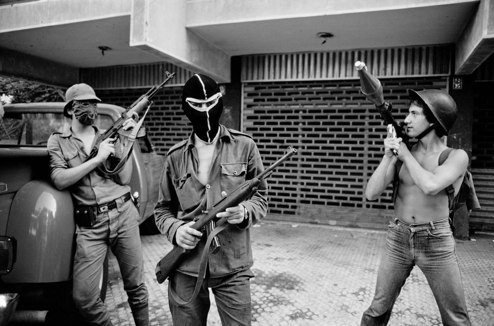 s/w Bild von drei Männern, zT vermummt, die mit ihren Waffen posieren