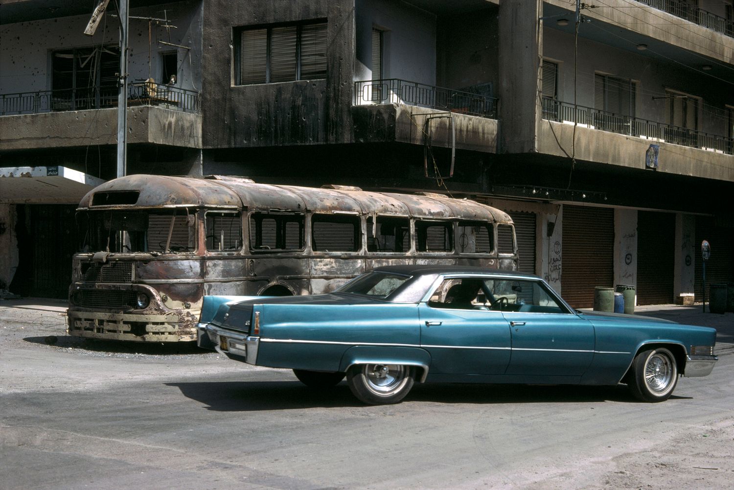 ein amerikanischer Cadillac vor einem ausgebrannten Bus