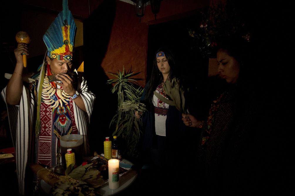 Ein Shaman mit Federkopfschmuck, Flöte und Rassel während der Ayahuasca-Zeremonie.  
