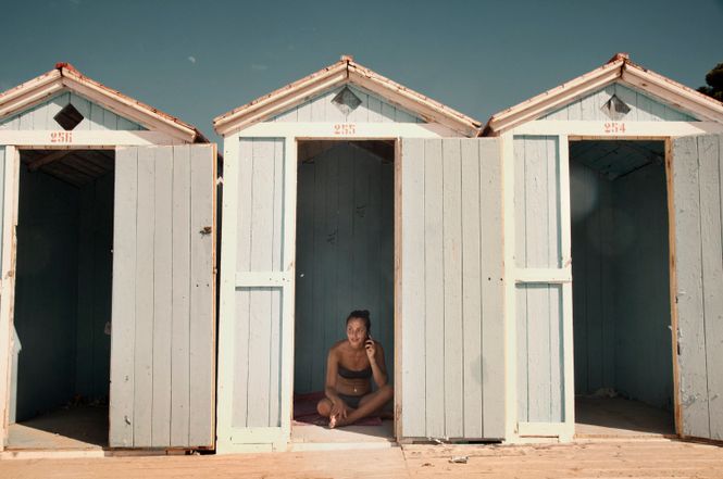 eine Frau sitzt in einem Badehäuschen am Meer und telefoniert