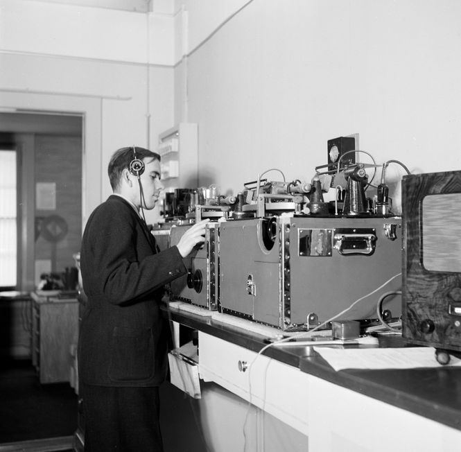 Die historische schwarz-weiss Fotografie zeigt einen Mann mit Kopfhörern im Radiostudio.