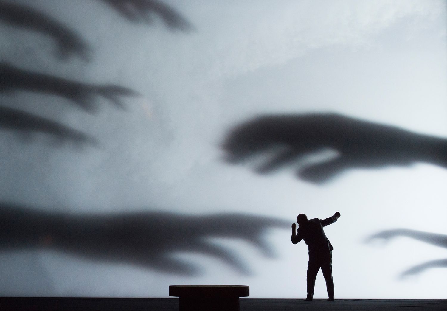 Expressionistisches Bühnenbild. Im Vordergrund Alviano Salvago, an der Wand Schatten von riesigen, bedrohlichen Händen. 