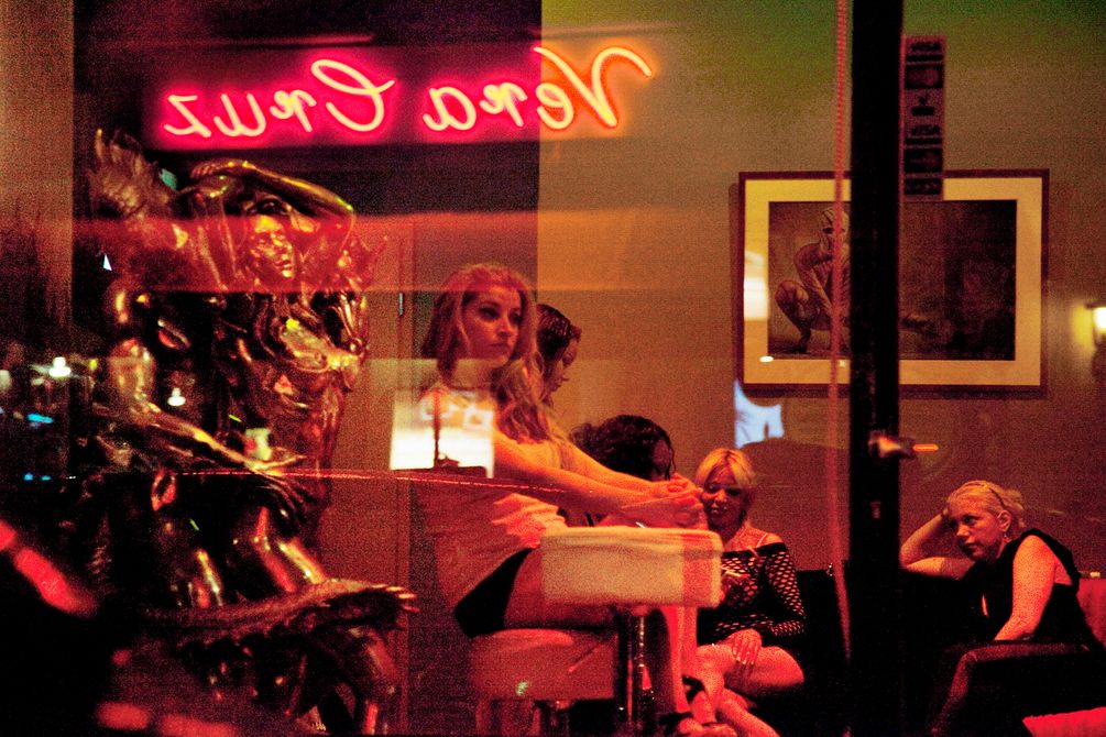Blick durschs Fenster in eine Bar, wo mehrere Prostituierte zusammensitzen und miteinander sprechen