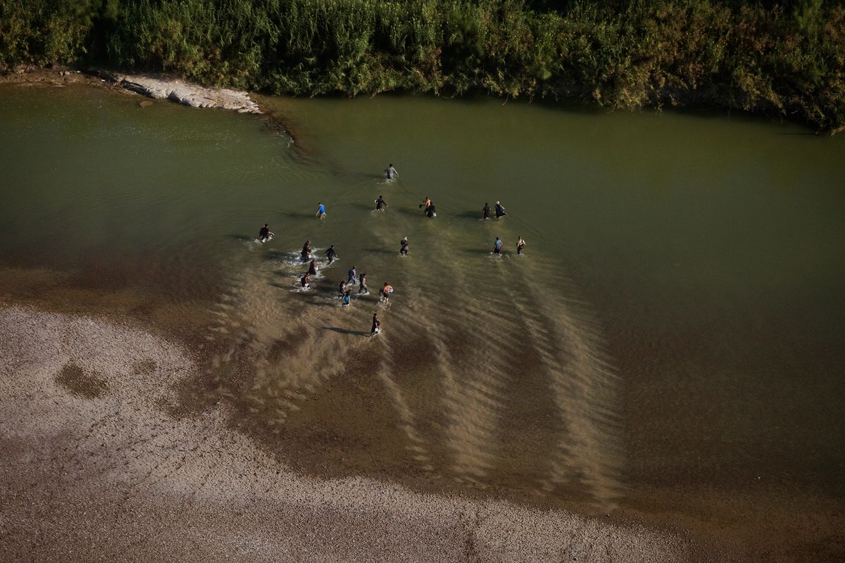 eine Gruppe von Flüchtlingen überquert einen seichten Fluss