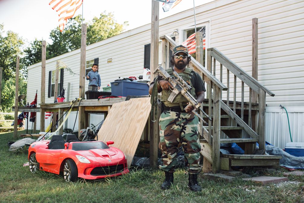 KKK mit halbautomatischen Gewehr und in Tarnmontour vor seinem Trailer