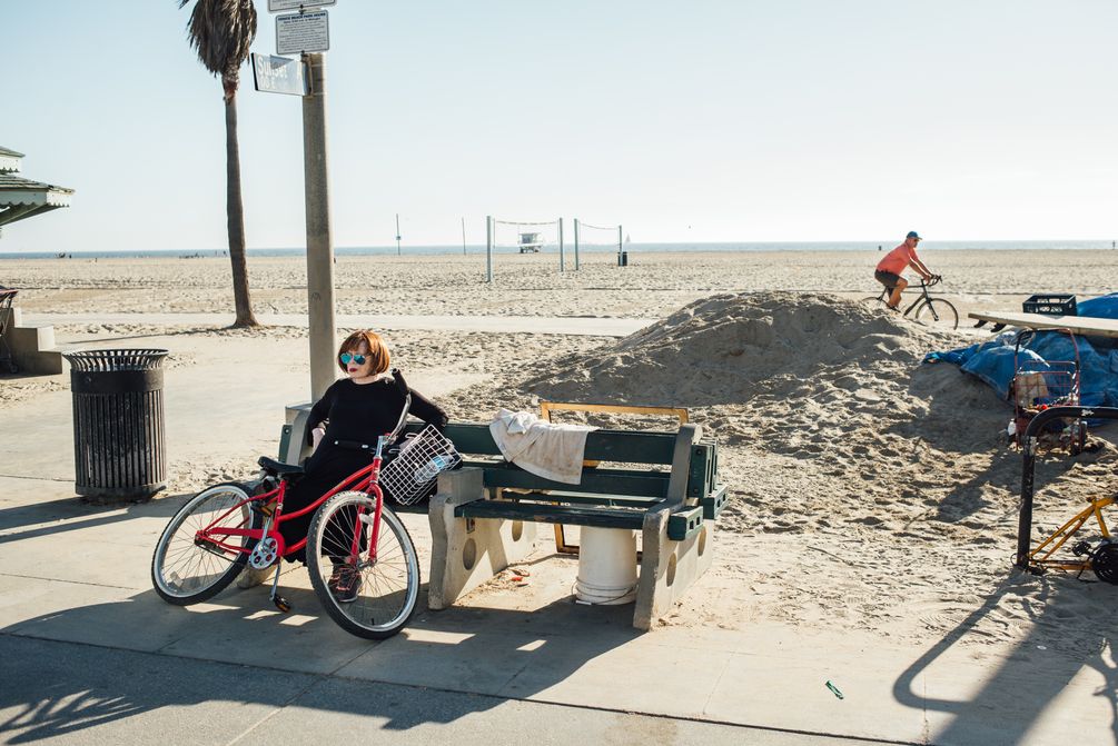 Ein Frau sitzt auf einer Bank am Strand, ihr Fahrrad angelehnt